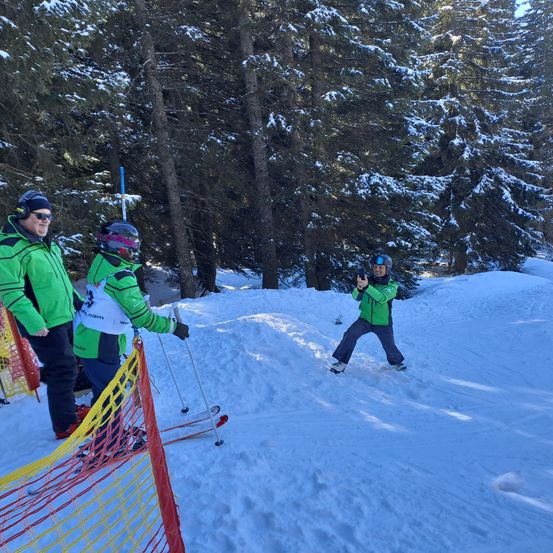 Eine Gruppe von Menschen beim Skifahren in einem verschneiten Gebiet mit Kiefern. Eine Person macht ein Foto.