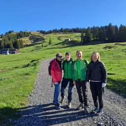 Vier Personen stehen auf einem Schotterweg in einer bergigen Region, alle in Winterkleidung. Zwei Frauen und zwei Männer lächeln für die Kamera.
