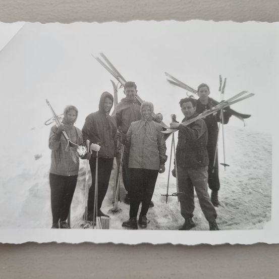 Ein Schwarz-Weiß-Foto von fünf Menschen in Winterkleidung, die im Schnee stehen und Skistöcke und Skier halten.