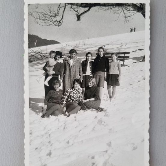Ein Schwarz-Weiß-Foto einer Familie, die in einem verschneiten Feld mit einer Bank im Hintergrund steht.