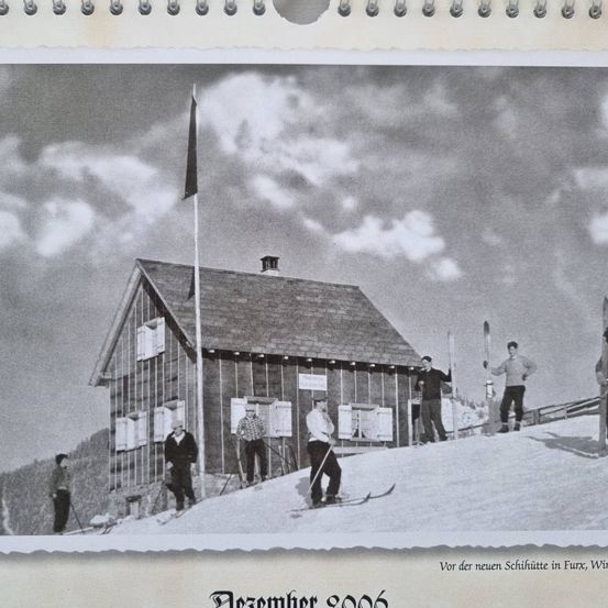 Schwarz-Weiß-Foto von Menschen in Winterkleidung, die vor einer Skihütte mit einer Fahne auf Schnee stehen. Unten steht der Datumsvermerk 'Dezember 1966'.