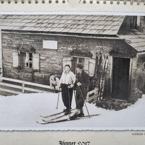 Ein Schwarz-Weiß-Foto von drei Personen auf Skiern vor einem Backsteinhaus mit verschneiltem Dach und einem Fenster mit weißen Fensterläden. Das Foto hat ein Datum von Januar 1917.