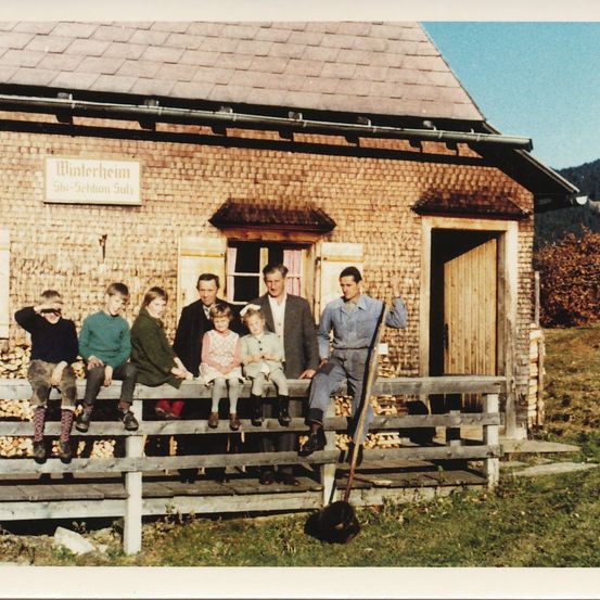 Eine Gruppe von Menschen, einschließlich Kindern, sitzt auf einem Holzzaun vor einem Backsteingebäude namens Winterheim.