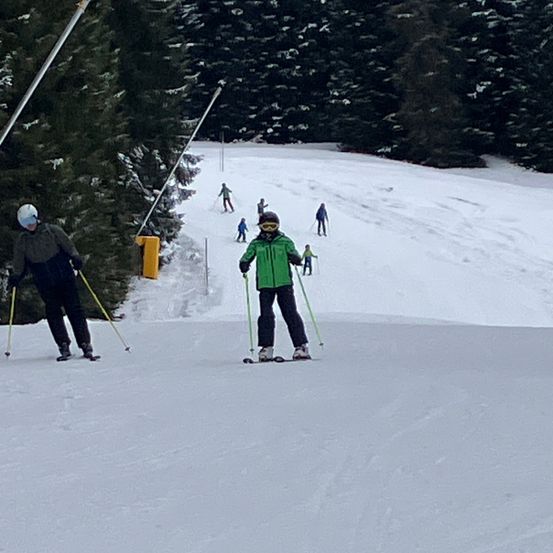 Eine Gruppe von Skifahrern auf einem verschneiten Hang, einige mit Helmen und Brillen, skifahren mit Skistöcken in der Hand.