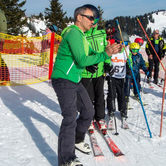 Ein Skifahrer mit der Nummer 67 erhält von einem Erwachsenen auf einem verschneiten Hang Anweisungen.