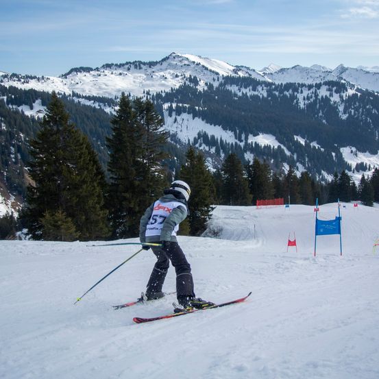 Ein Skifahrer mit der Startnummer 57 navigiert einen verschneiten Hang mit Bergen im Hintergrund.