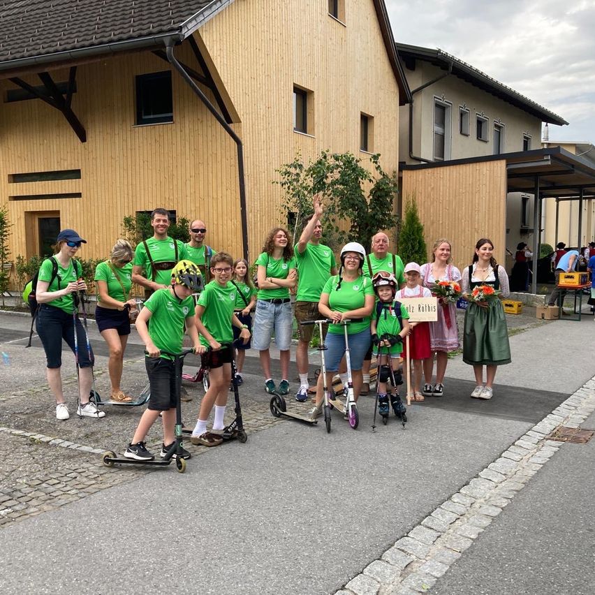 Eine Gruppe von Menschen in grünen Shirts, Helmen und Sneakers posiert für ein Foto vor einem Gebäude an einem sonnigen Tag.