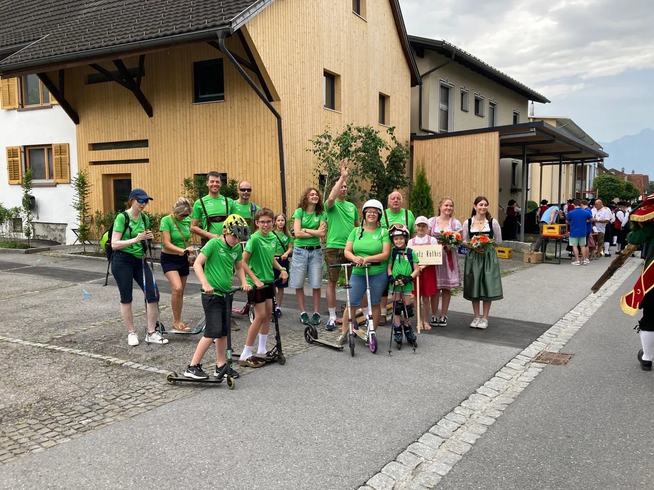 Eine Gruppe von Menschen in grünen Shirts, Helmen und Sneakers posiert für ein Foto vor einem Gebäude an einem sonnigen Tag.