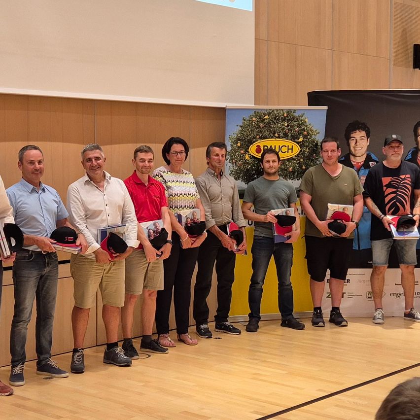 Eine Gruppe von Männern steht in einer Reihe und hält Bücher und Hüte in der Hand. Sie befinden sich in einem Raum mit Holzböden und einer gelben Wand mit einem Plakat.