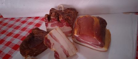 Mehrere Scheiben geräuchertes Fleisch sind auf einer weißen Oberfläche angeordnet, mit einem rot-weiß karierten Tuch darunter. Das Fleisch ist in verschiedene Formen und Größen geschnitten.