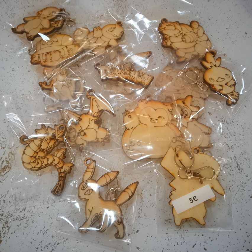 Several wooden keychains of various Pokemon characters, each individually packaged in clear plastic bags. The keychains include Pikachu, Eevee, and others, with one keychain priced at 5 euros.