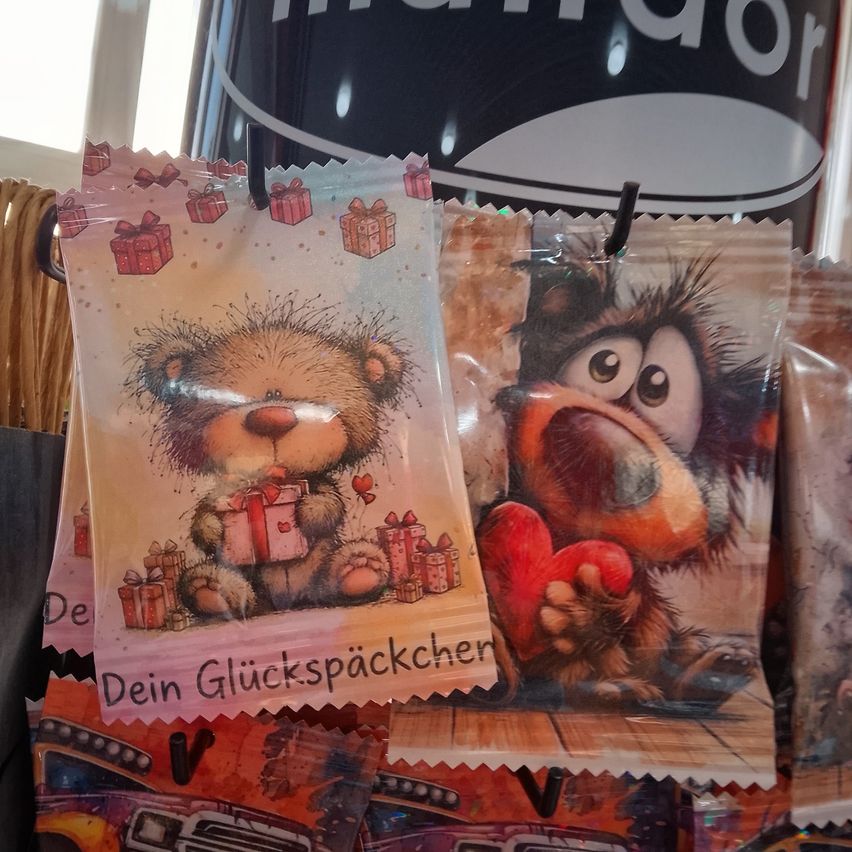 Two small bags of fortune cookies hang on a hook, one featuring a bear holding a gift and the other a creature holding a heart.