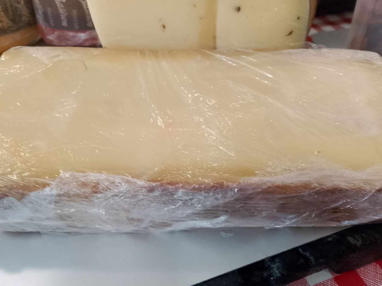 A close-up of a block of cheese wrapped in plastic, resting on a white surface.