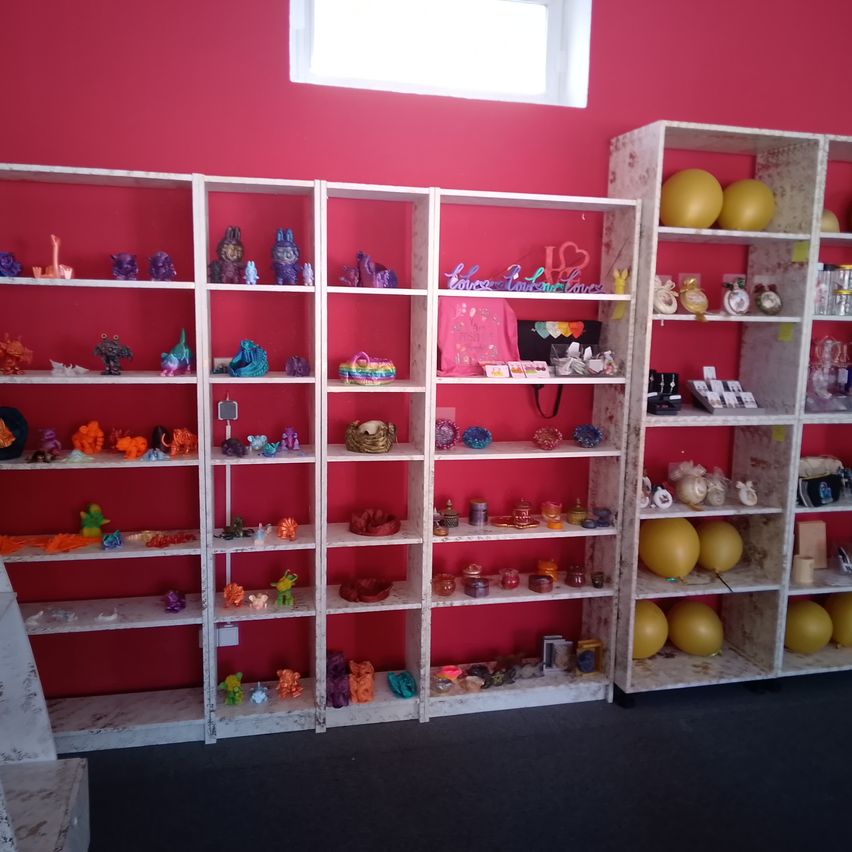 Ein Raum mit Regalen, die mit farbigen Gegenständen an einer roten Wand gesäumt sind. Die Regale enthalten Figuren, Dekorationsgegenstände und Ballons.
