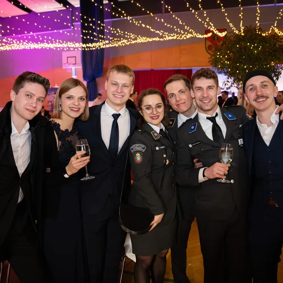 Eine Gruppe von Menschen in Militäruniformen und Abendkleidung posiert für ein Foto mit Getränken in den Händen in einem dekorierten Raum.