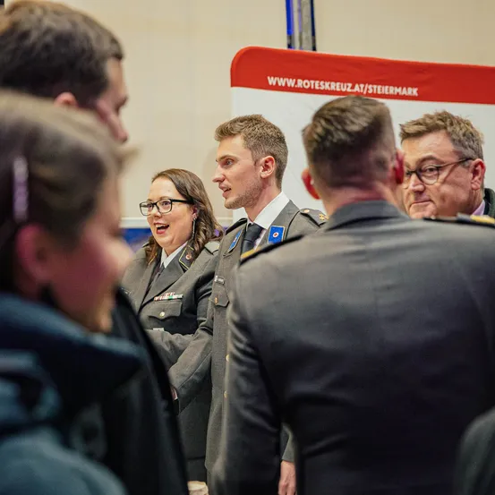 Eine Gruppe von Militärangehörigen führt eine Diskussion. Eine Frau mit Brille und ein Mann in Uniform sprechen mit anderen.