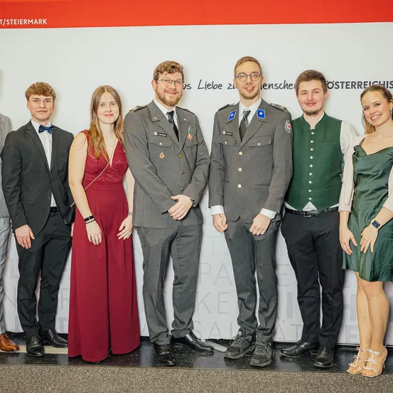 Gruppe von Menschen, die für ein Foto zusammenstehen. Zwei Männer in Uniformen, einer in Militär- und der andere in traditioneller Kleidung. Drei Frauen und ein Mann in formeller Kleidung. Sie alle lächeln.