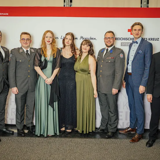 Eine Gruppe von Menschen in Uniformen und Anzügen posiert für ein Foto vor einem weißen Banner mit rotem Text.