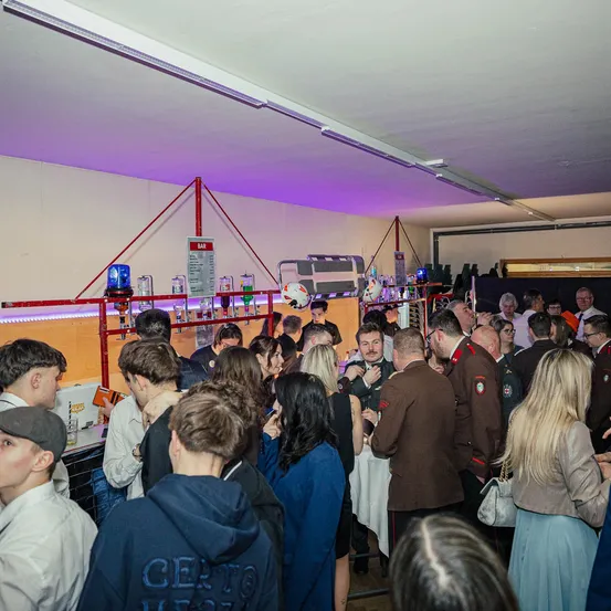 Eine große Indoor-Veranstaltung mit einer Gruppe von Menschen in Uniformen und Hüten, wahrscheinlich bei einer formellen Zusammenkunft oder Feier. Eine Bar ist vorhanden, und einige Personen trinken und unterhalten sich.