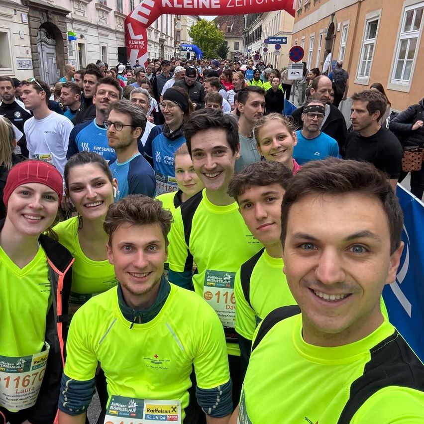 Marathonteilnehmer in neongrünen Shirts stehen lächelnd zusammen für ein Foto vor einem Bogen.