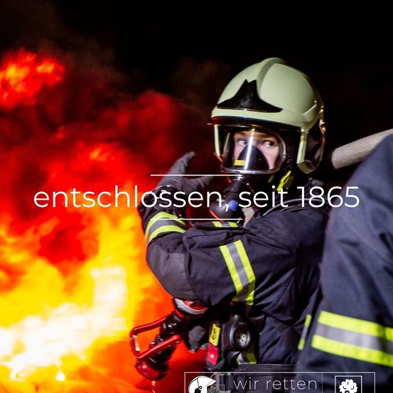 Ein Feuerwehrmann mit Helm und Maske steht vor einem brennenden Feuer. Der Text 'entschlossen, seit 1865' ist in der Mitte des Bildes angezeigt.