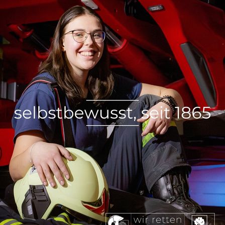 Eine Frau in einer Feuerwehruniform sitzt neben einem gelben Helm. Sie lächelt. Der Text im Bild lautet 'Selbstbewusst seit 1865'. Es gibt einen roten und schwarzen Hintergrund.