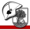 Ein heraldisches Emblem zeigt einen Feuerwehrhelm, einen Baum und ein Fass. Der Baum wächst aus dem Fass, das mit Schutt gefüllt ist. Der Schild ist mit einem roten Streifen umrandet.