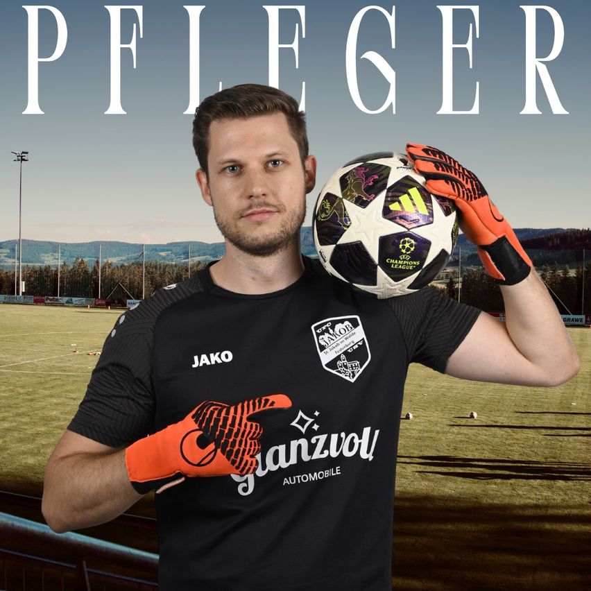 A soccer player in a black jersey with 'Jako' and 'Ganzvoll Automobile' logos holds a soccer ball and orange gloves in front of a sports field.