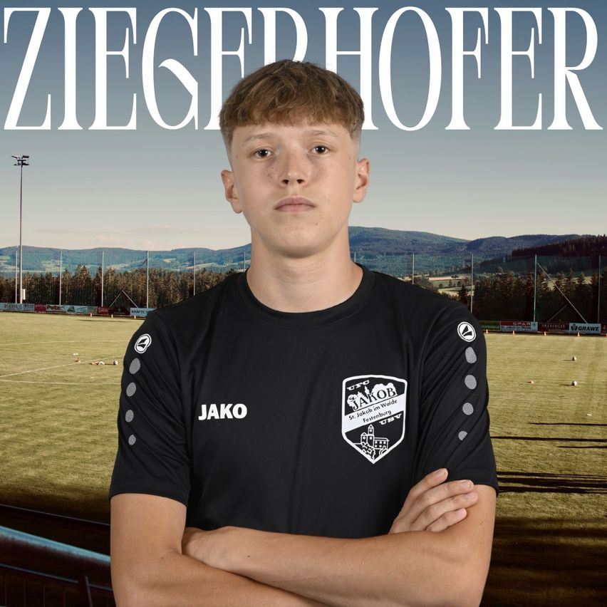 A young man stands in front of a soccer field, wearing a black Jako jersey with a logo on the chest. The background features a blurred image of a soccer field with mountains in the distance.