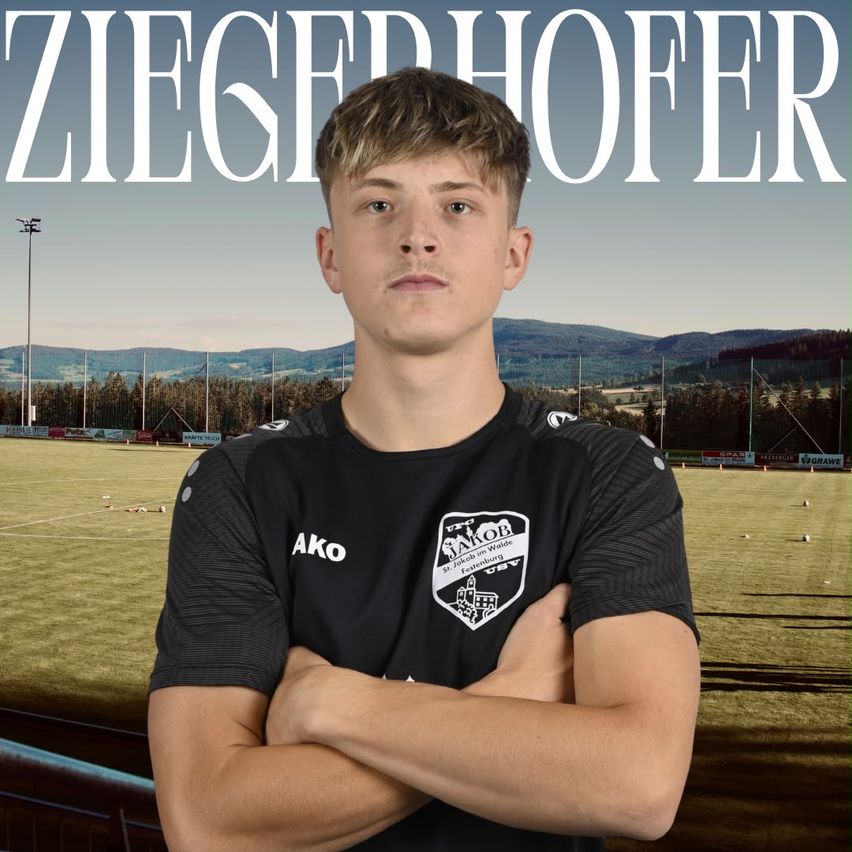 A young man in a black soccer jersey with the word 'AKO' on it stands with his arms crossed in front of a blurred soccer field.
