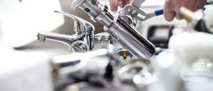 Ein Klempner benutzt eine Zange an einem Badezimmerhahn, mit anderen Klempnerwerkzeugen und einem Waschbecken im Hintergrund.