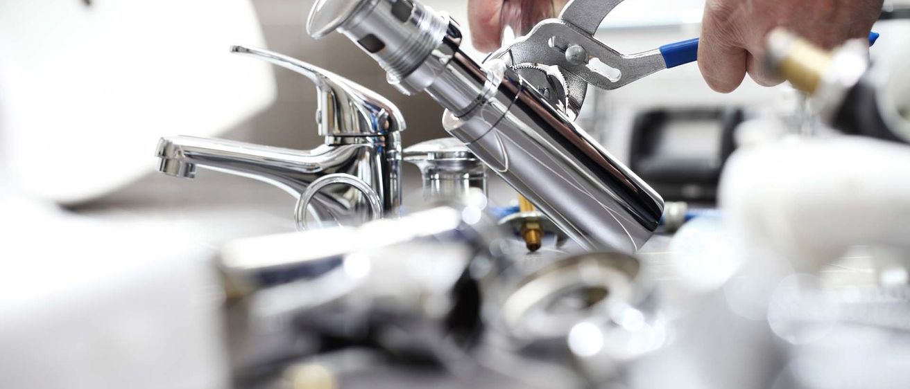Ein Klempner benutzt eine Zange an einem Badezimmerhahn, mit anderen Klempnerwerkzeugen und einem Waschbecken im Hintergrund.