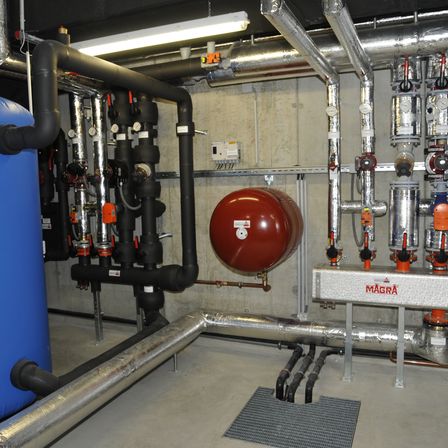 Eine industrielle Anlage mit verschiedenen Rohren und einem zentralen roten Tank, beschriftet mit 'MAGRA', umgeben von zahlreichen Ventilen und Sensoren.