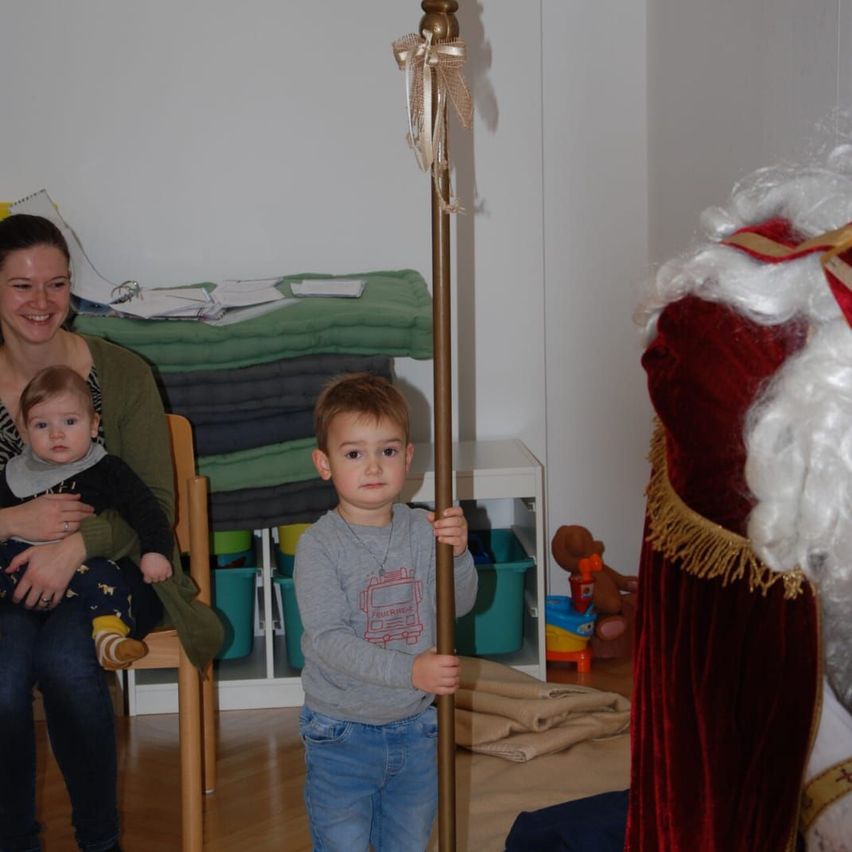 Eine Frau, die ein Baby hält, und ein junger Junge, der einen goldenen Stab hält, stehen neben einer Person, die als Weihnachtsmann verkleidet ist.