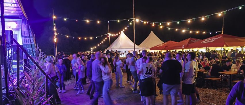 A nighttime outdoor event with people dancing and socializing under string lights and tents.