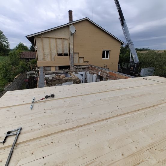 Ein Haus im Bau mit einem Kran in der Nähe. Holzdielen sind auf dem Boden verlegt, mit Werkzeug darauf.