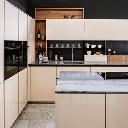 Eine moderne Küche mit weißen Schränken, schwarzen Arbeitsplatten und einem hölzernen Regal mit verschiedenen Gegenständen. Die Küche verfügt über einen schlanken Waschbecken und einen Wasserhahn sowie einen Gasherd.