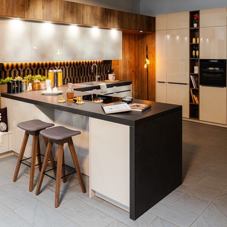 Eine moderne Küche mit Holzschränken, schwarzen Arbeitsplatten und einer hölzernen Insel mit Stühlen. Sie verfügt über ein Waschbecken, Herd und Backofen sowie Regale mit Pflanzen und Büchern.