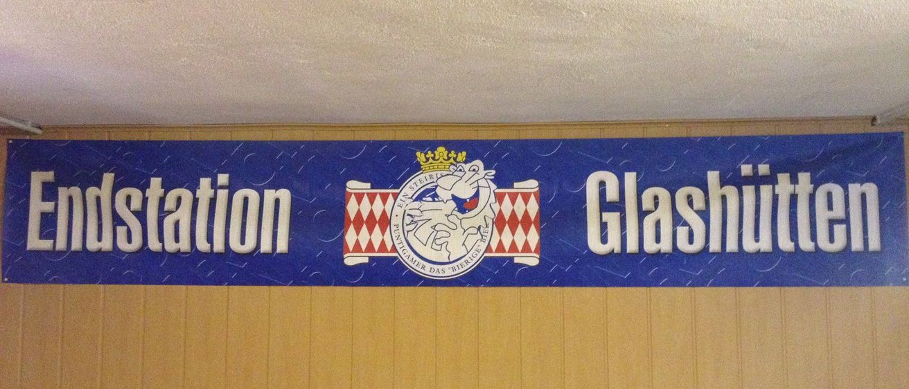 Ein blaues Banner zeigt links 'Station' und rechts 'Glashut', mittig ein Logo.