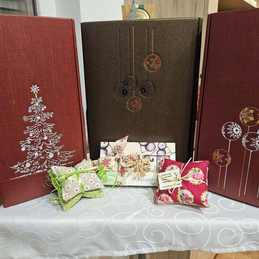 A collection of gift boxes, one with a Christmas tree design, another with a decorative ornament, and a small pillow with a tag on a white tablecloth.