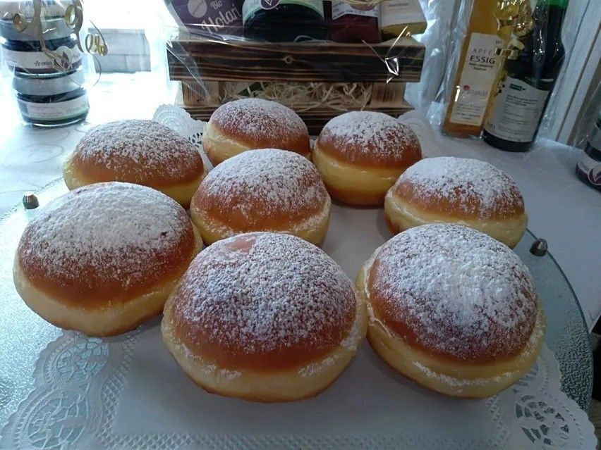 Ein Teller mit Donuts, die mit Puderzucker bestreut sind, steht auf einem Tisch mit verschiedenen Flaschen und einem Korb.