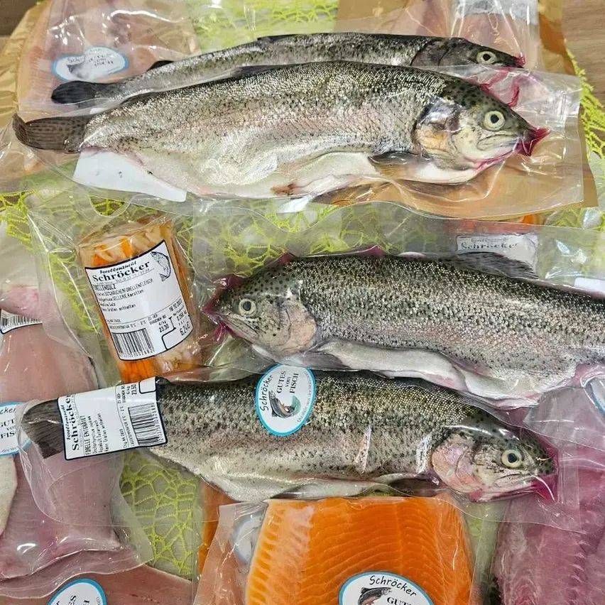 Various fish, including trout, are neatly arranged in clear plastic bags. Some are whole, others are filleted. Each fish has a label and is accompanied by slices of salmon.