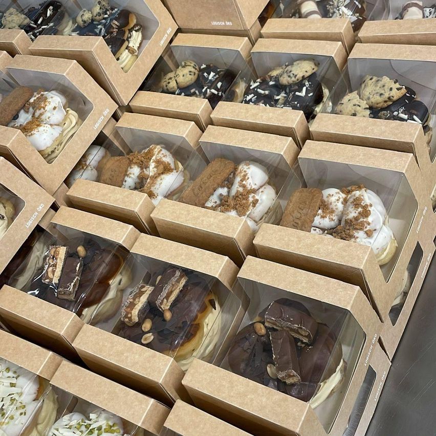 A variety of desserts in brown boxes, each containing multiple pastries. The pastries include chocolate, vanilla, and cookies. Each box has a transparent cover, showing the contents.