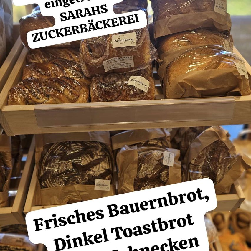 Display of assorted breads including rolls, toast, and rye bread, with labels indicating 'Fresh Farmer Bread, Dinkel Toast Bread, and Black Rye Bread'. Breads are wrapped in paper and plastic, some with white tags.