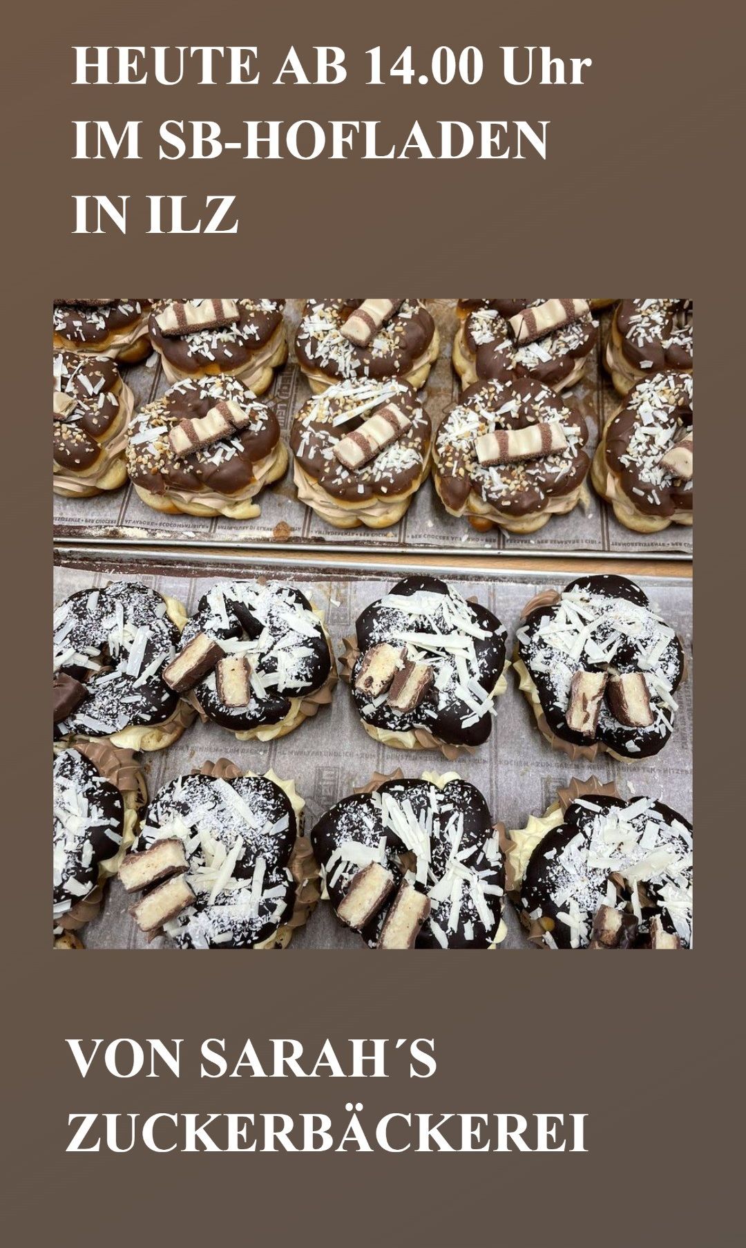 Eine Auswahl an mit Schokolade überzogenen Donuts mit verschiedenen Toppings, darunter Kit Kats und Kokosnuss, ist in zwei Reihen auf Tabletts angeordnet.