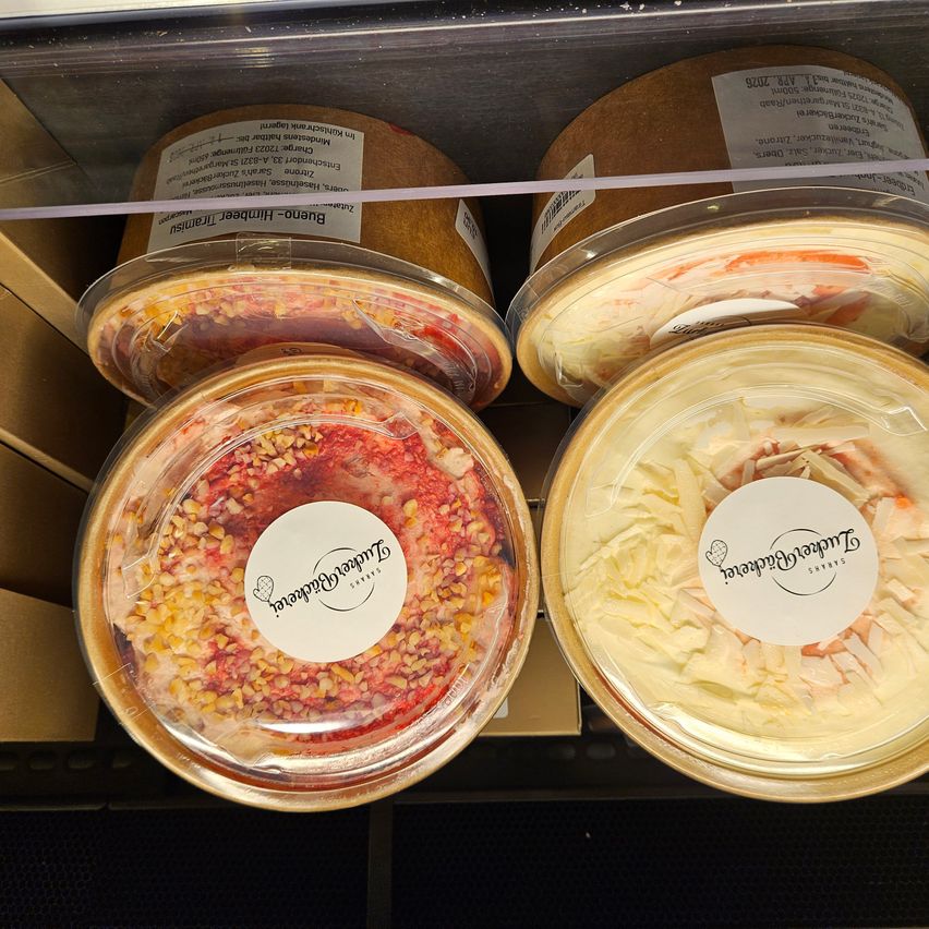 Four containers of different food products are displayed in a glass case. Each container is covered with plastic and has a white label on the front.