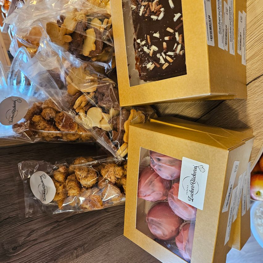 Various boxes of desserts on a wooden surface. One box contains chocolate-covered items with nuts, while another has pink-frosted pastries.