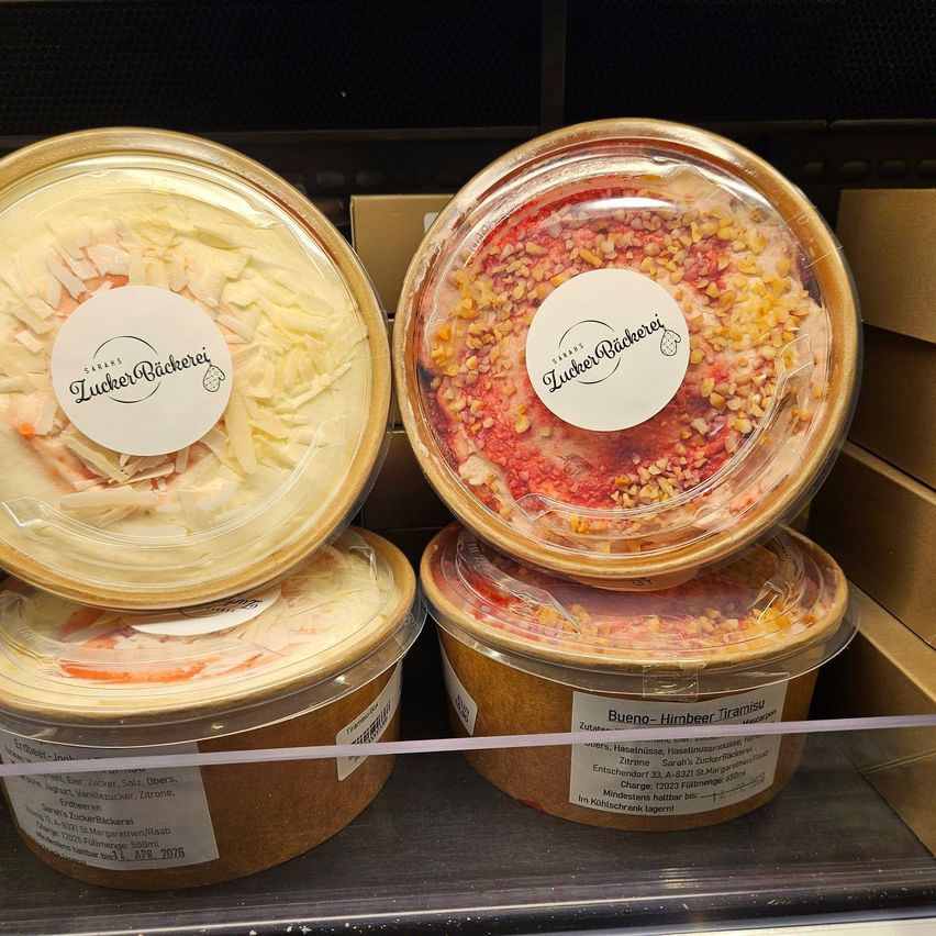 Four containers of Lucker Backerei desserts, each with distinct toppings, are displayed on a shelf. Each container has a label with the brand name and details about its contents.