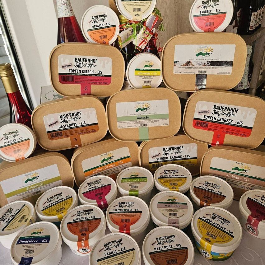 A variety of ice creams with various flavors are displayed, including Topfen Kirsch, Haselnuss, and Schoko-Banane. They are packed in boxes with labels and some are in tubs.