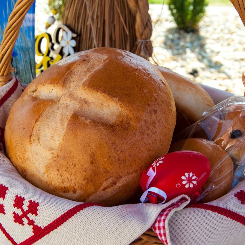 Ein Korb mit Brot und einem roten Ei mit weißen Blumen darauf. Das Brot ist braun mit einem Kreuzdesign.